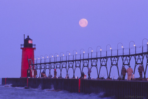 Fishermen looking at the setting full moon on the South Haven, Michigan pier.